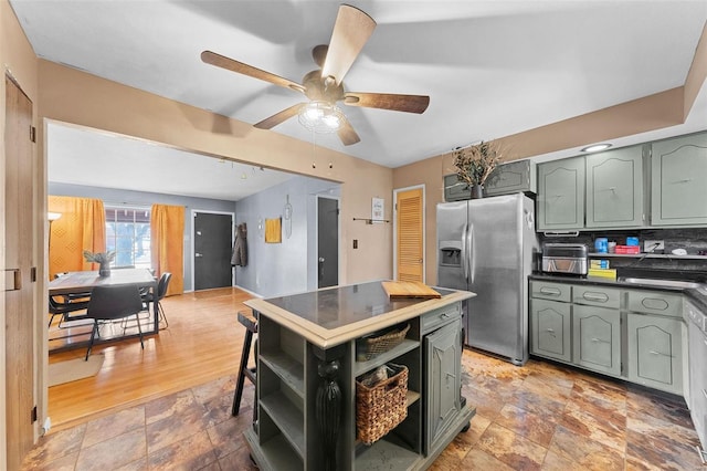 kitchen with open shelves, stone finish flooring, dark countertops, stainless steel fridge, and green cabinets