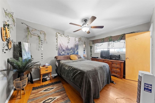 bedroom with heating unit, ceiling fan, baseboards, and light wood-style floors