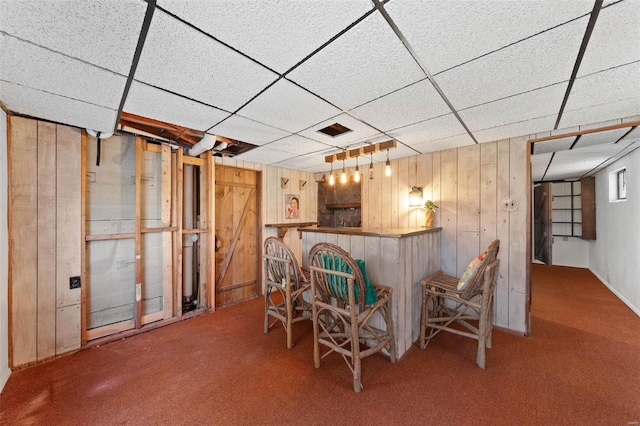 bar with a drop ceiling, wooden walls, a dry bar, and carpet flooring