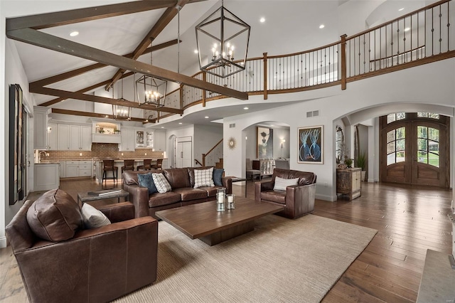 living room featuring an inviting chandelier, arched walkways, high vaulted ceiling, stairs, and visible vents