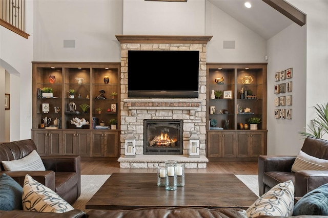 living room with arched walkways, a fireplace, wood finished floors, and high vaulted ceiling