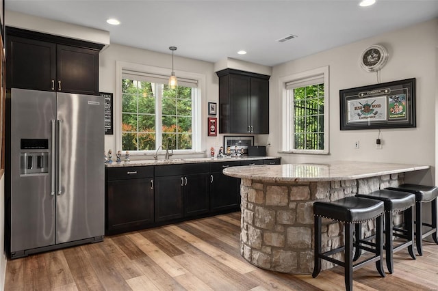 kitchen featuring a peninsula, high end fridge, light wood-style floors, light stone counters, and a sink