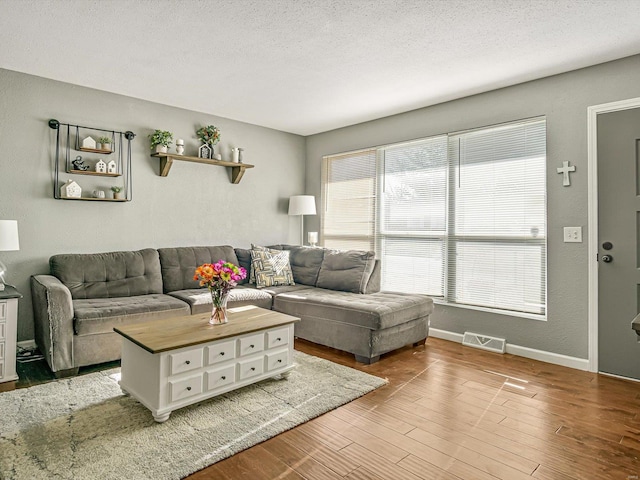 living room with visible vents, baseboards, wood finished floors, a textured wall, and a textured ceiling