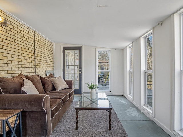 living room featuring baseboards, concrete flooring, brick wall, and an accent wall