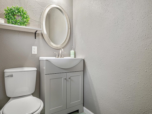 half bathroom with toilet, vanity, and a textured wall