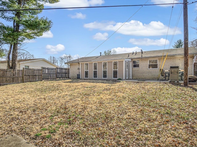 back of property with brick siding, a lawn, a patio, and fence