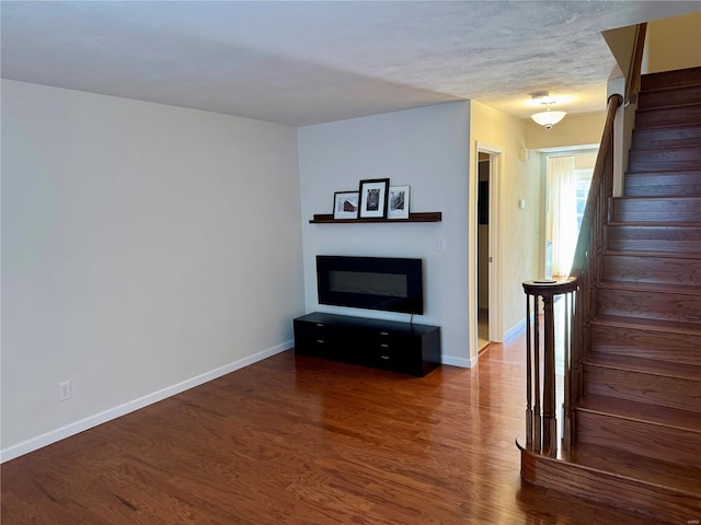 unfurnished living room with stairway, baseboards, and wood finished floors