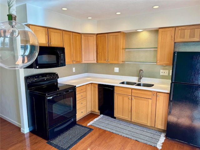 kitchen featuring light wood finished floors, light countertops, recessed lighting, black appliances, and a sink