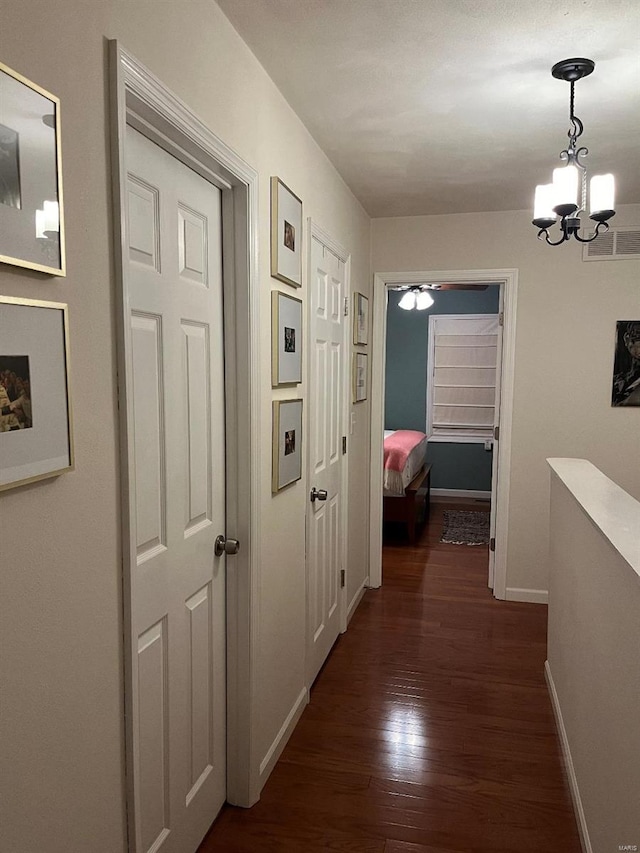 hallway with visible vents, baseboards, a notable chandelier, and dark wood finished floors