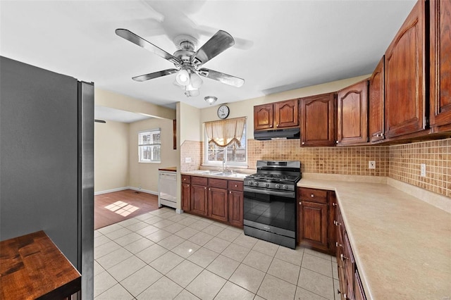 kitchen with under cabinet range hood, stainless steel appliances, light tile patterned flooring, light countertops, and decorative backsplash