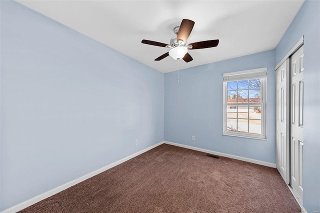 unfurnished bedroom with a ceiling fan, visible vents, baseboards, a closet, and dark colored carpet