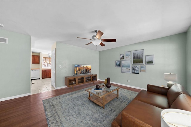 living room with ceiling fan, visible vents, baseboards, and light wood-style flooring