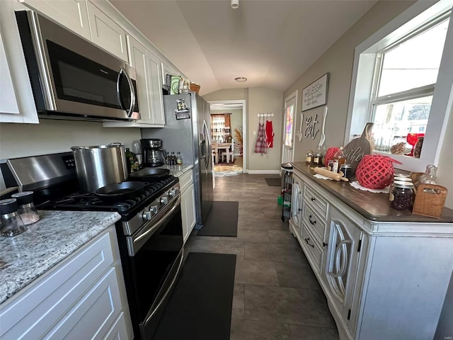 kitchen featuring baseboards, white cabinets, appliances with stainless steel finishes, light stone counters, and vaulted ceiling