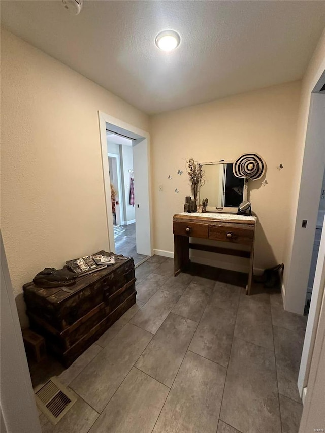 corridor with a textured ceiling, visible vents, and baseboards