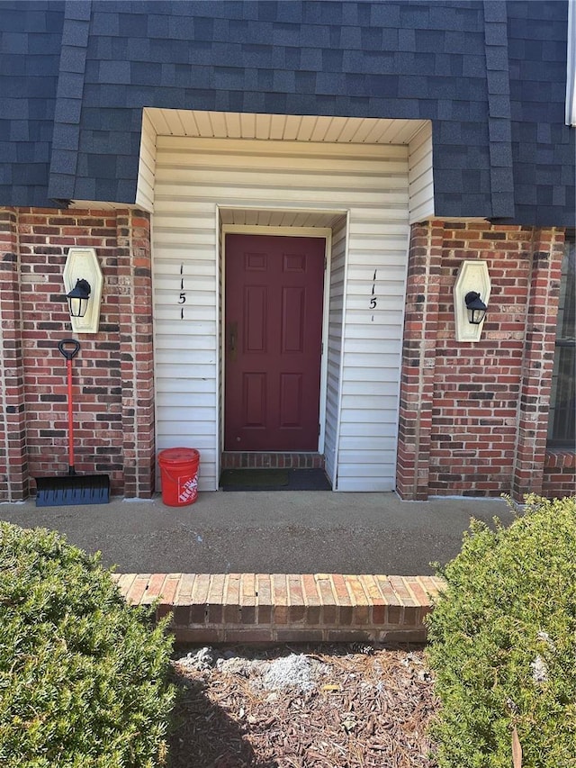 doorway to property with a shingled roof, brick siding, and mansard roof