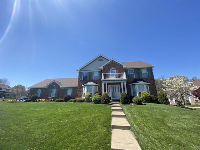 colonial inspired home with brick siding, a balcony, and a front lawn