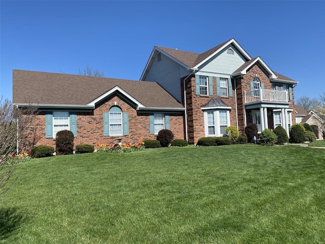 view of front of property featuring brick siding, a balcony, a front lawn, and roof with shingles