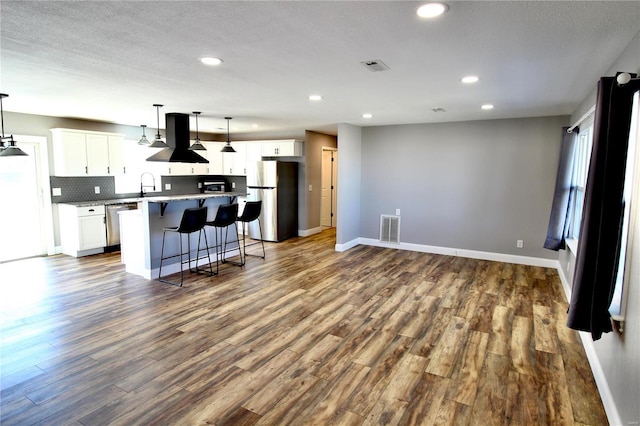 kitchen with a breakfast bar area, visible vents, appliances with stainless steel finishes, white cabinets, and ventilation hood