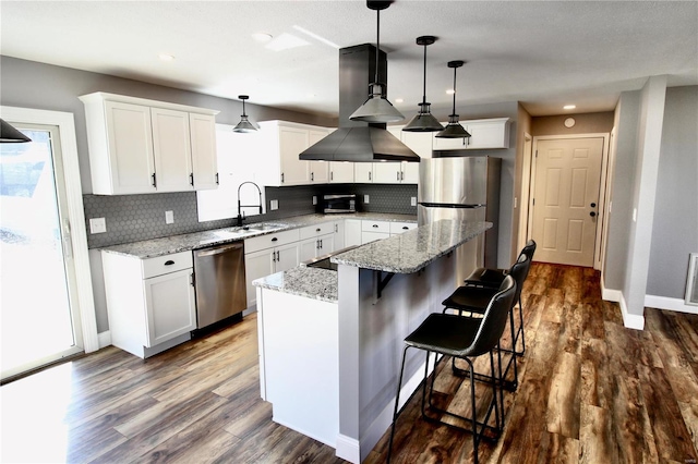 kitchen with island exhaust hood, appliances with stainless steel finishes, dark wood-type flooring, a sink, and a kitchen island