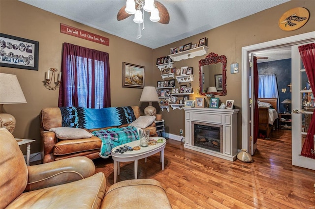 living area with a glass covered fireplace, a textured ceiling, ceiling fan, and wood finished floors