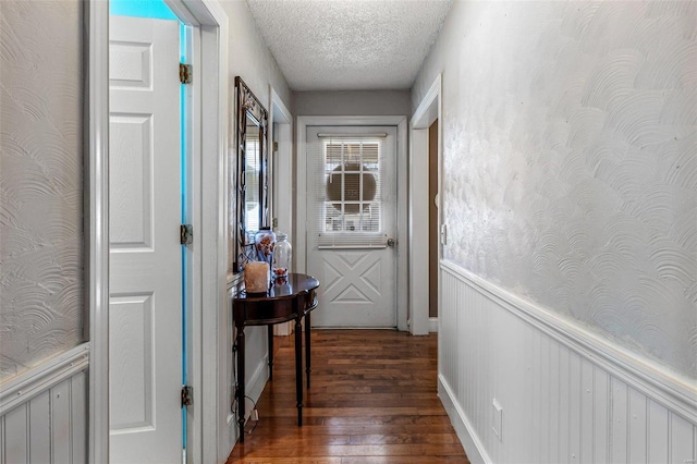 doorway to outside featuring a textured ceiling, hardwood / wood-style floors, wainscoting, and wallpapered walls