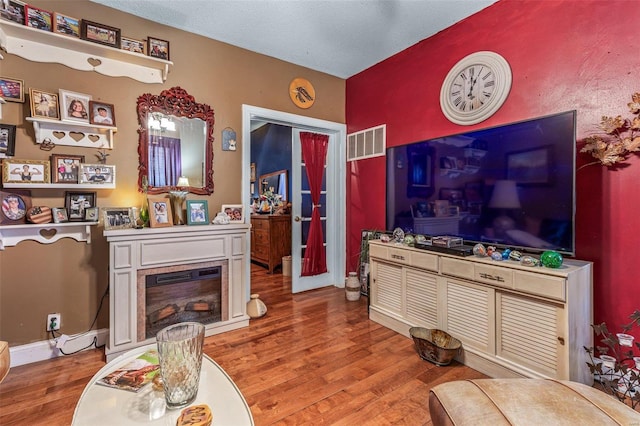 living area with wood finished floors, visible vents, baseboards, a textured ceiling, and a glass covered fireplace