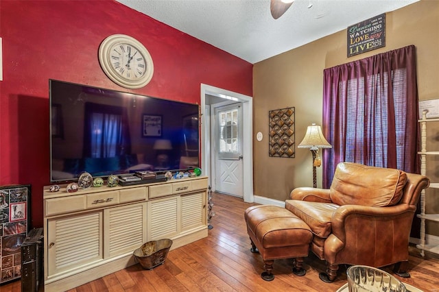 living area with hardwood / wood-style flooring, a ceiling fan, baseboards, and a textured ceiling