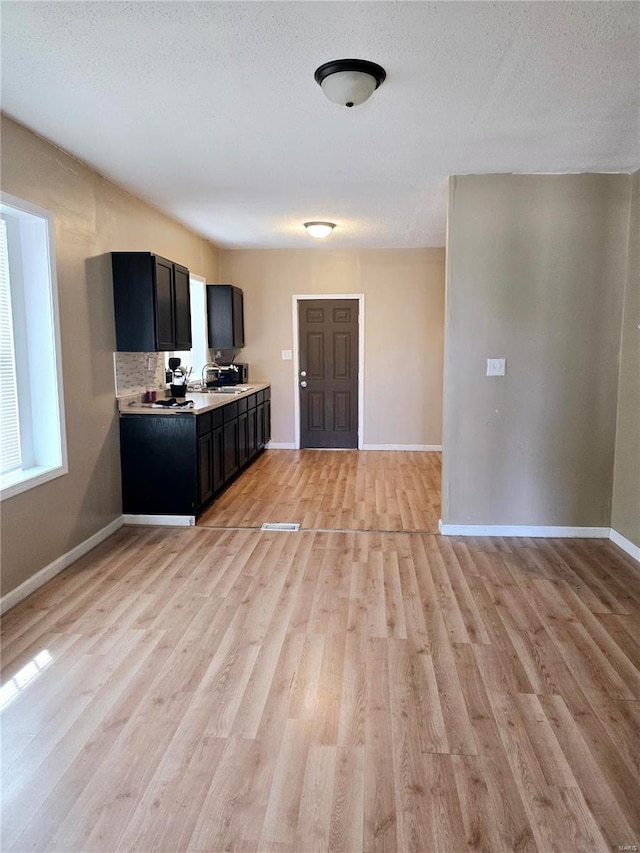 kitchen featuring baseboards, light countertops, decorative backsplash, light wood-style floors, and dark cabinets