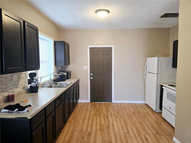 kitchen with a sink, light countertops, light wood-type flooring, white appliances, and dark cabinets