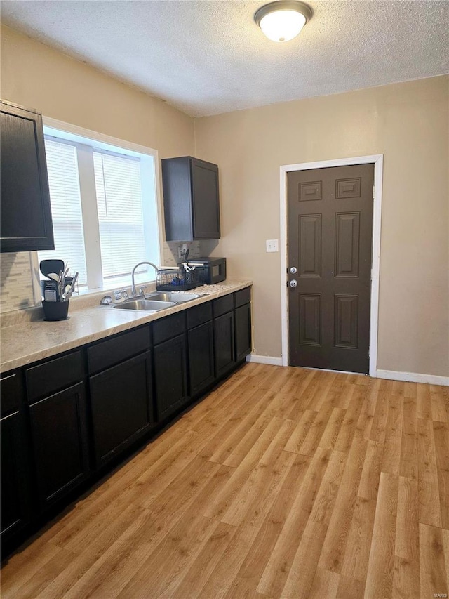 kitchen featuring black microwave, light countertops, light wood-style floors, a textured ceiling, and a sink