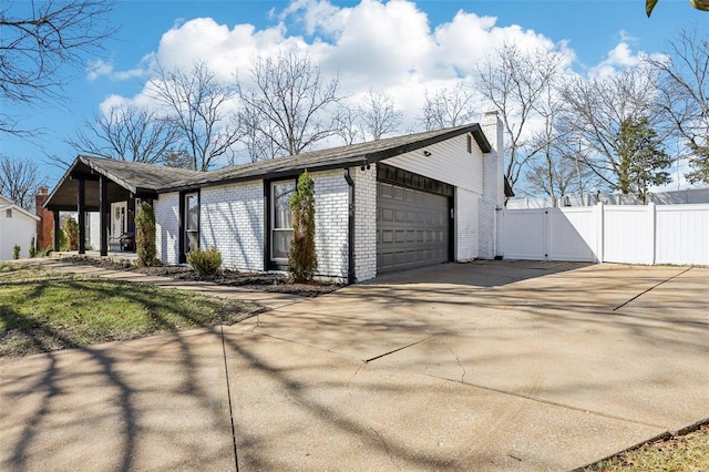 exterior space featuring a garage, concrete driveway, a gate, fence, and brick siding