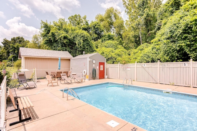 community pool featuring a patio, fence, and an outbuilding