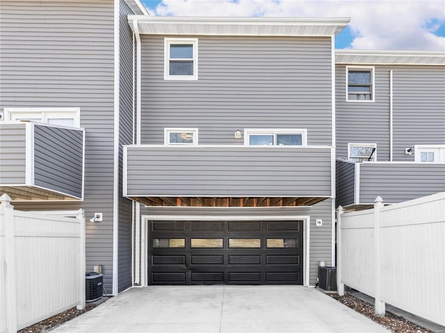 rear view of house featuring central air condition unit, a garage, driveway, and fence