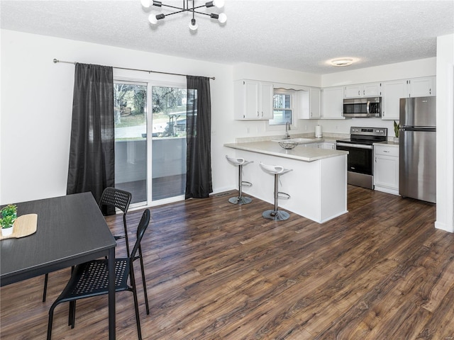 kitchen with dark wood-type flooring, a sink, appliances with stainless steel finishes, a peninsula, and light countertops