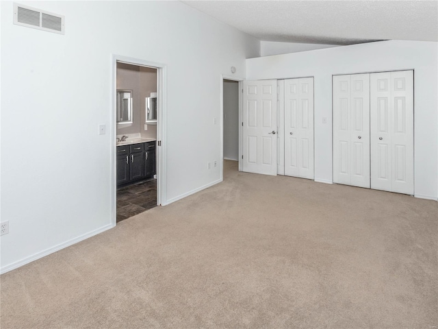 unfurnished bedroom with visible vents, multiple closets, connected bathroom, carpet floors, and vaulted ceiling