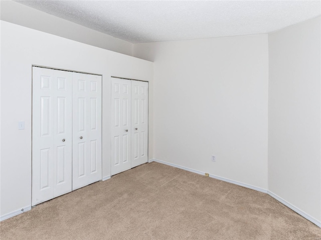 unfurnished bedroom with carpet flooring, baseboards, multiple closets, and a textured ceiling