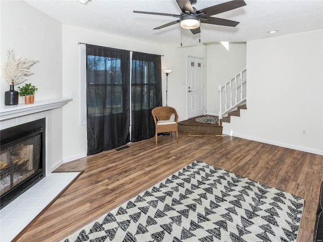 living room with visible vents, a tiled fireplace, a textured ceiling, wood finished floors, and stairs