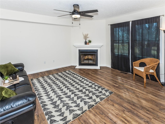 living room with visible vents, baseboards, a fireplace with flush hearth, wood finished floors, and a textured ceiling