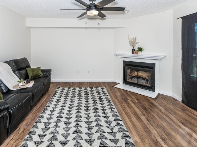 living area featuring a ceiling fan, wood finished floors, baseboards, a textured ceiling, and a tiled fireplace