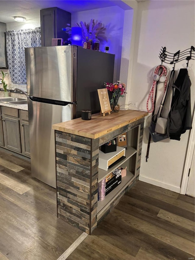 kitchen featuring baseboards, dark wood finished floors, freestanding refrigerator, a sink, and butcher block counters