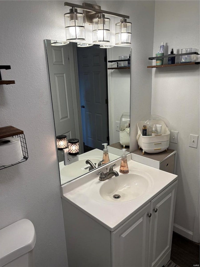 half bathroom featuring toilet, vanity, and a textured wall