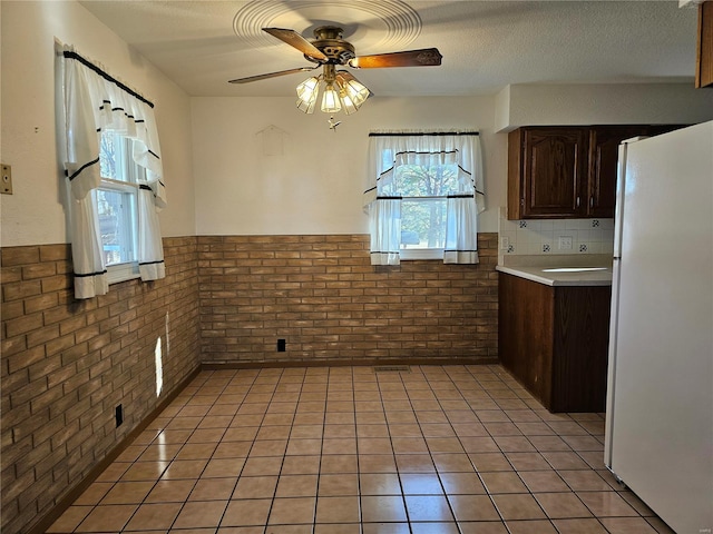 kitchen featuring brick wall, light tile patterned floors, wainscoting, freestanding refrigerator, and a textured ceiling