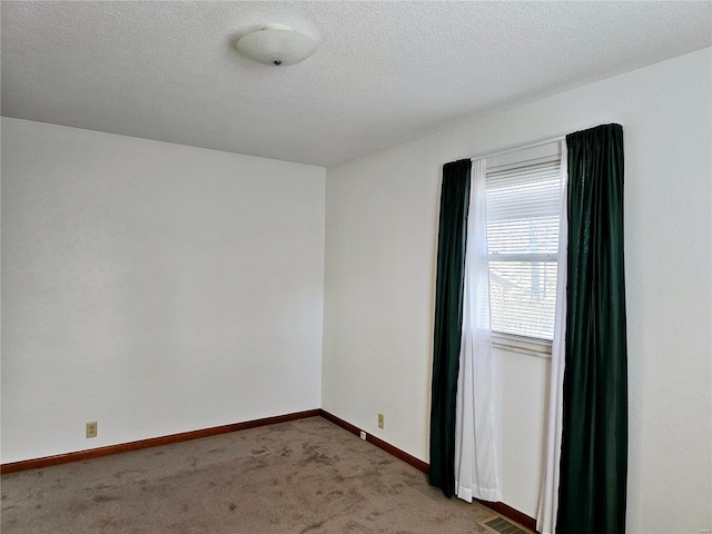 carpeted spare room featuring visible vents, baseboards, and a textured ceiling