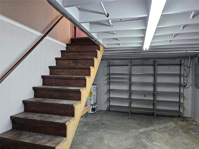 staircase with gas water heater, unfinished concrete floors, and electric panel