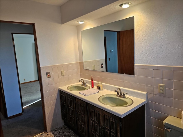 bathroom with double vanity, toilet, tile walls, and a sink