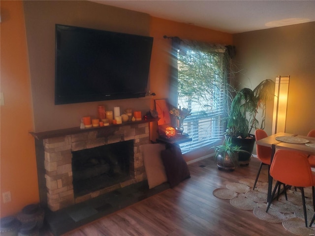 living area featuring a stone fireplace, baseboards, and wood finished floors