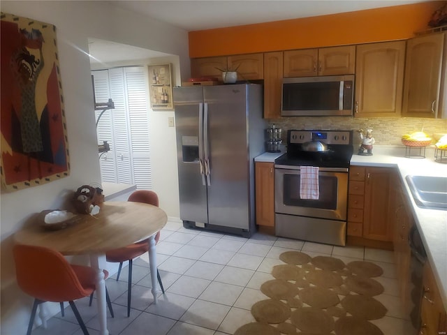 kitchen featuring light tile patterned floors, light countertops, backsplash, appliances with stainless steel finishes, and brown cabinetry