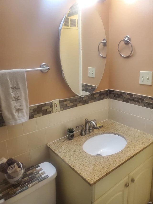 half bathroom with toilet, a wainscoted wall, tile walls, and vanity