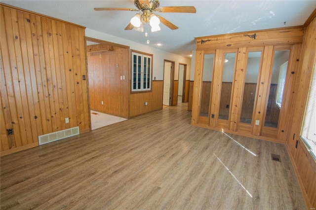 spare room featuring ceiling fan, wooden walls, visible vents, and wood finished floors