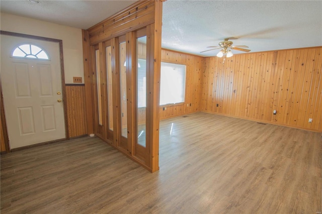 foyer with a textured ceiling, wood finished floors, a ceiling fan, and wooden walls